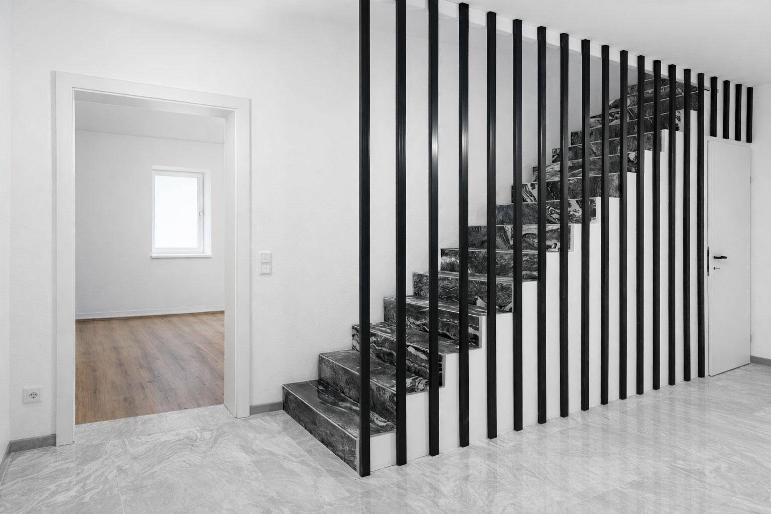 Moderner Flur mit eleganten Marmortreppen und schwarzer Lamellenabtrennung.