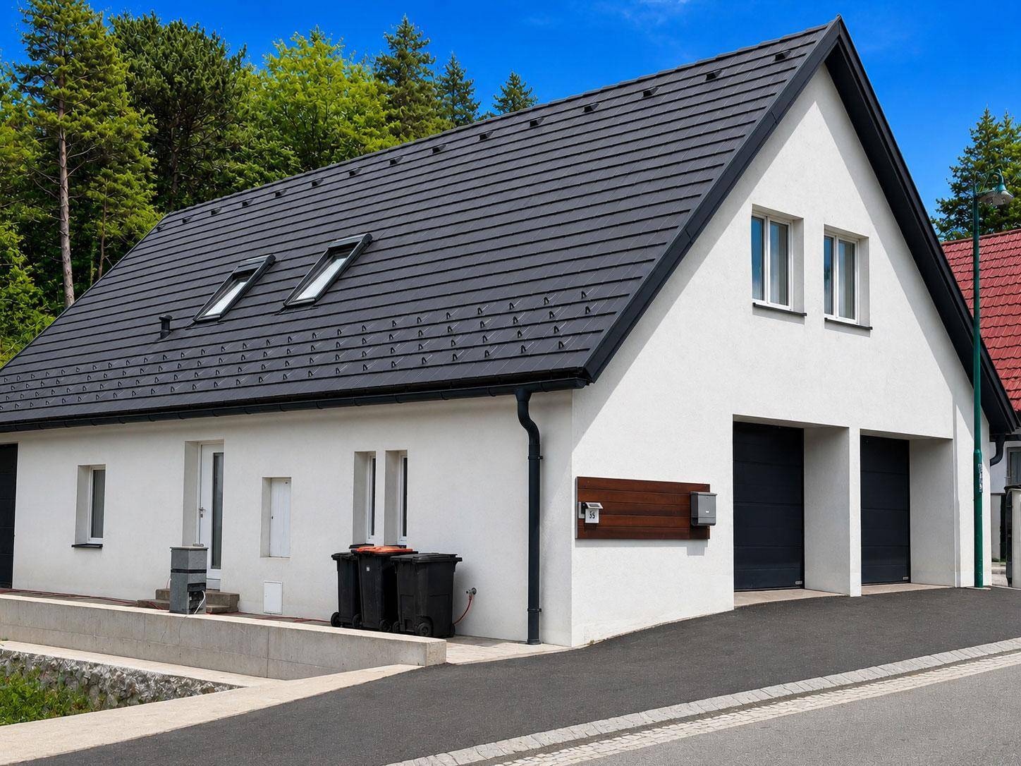 Seitenansicht des Hauses mit dunklem Satteldach, Dachfenstern und zwei Garagentoren.