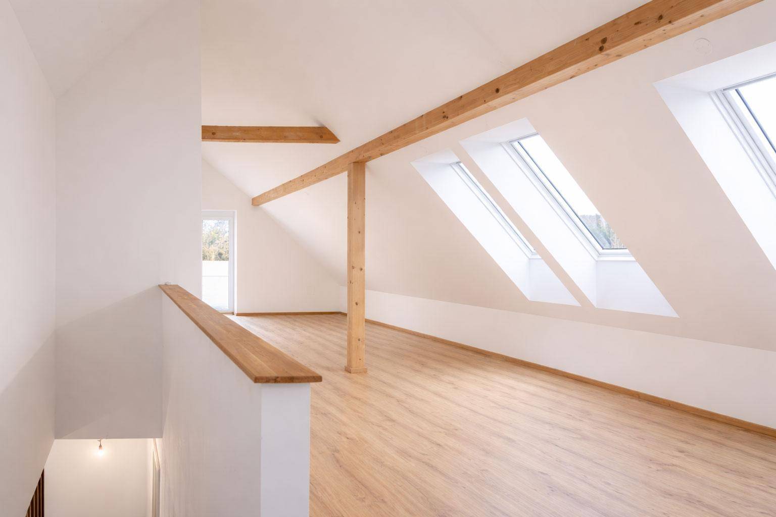 Geräumiger Dachbodenraum mit Holzbalken, Laminatboden und mehreren Dachfenstern.