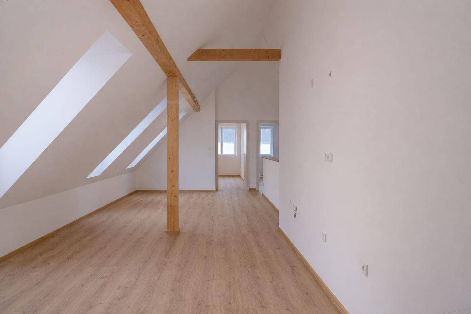 Offener Dachbodenbereich mit Holzbalken, Laminatboden und Blick in angrenzende Räume.