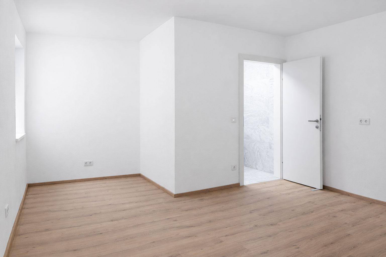 Leeres Zimmer mit hellem Laminatboden und weiß gestrichenen Wänden, bereit zur Einrichtung.