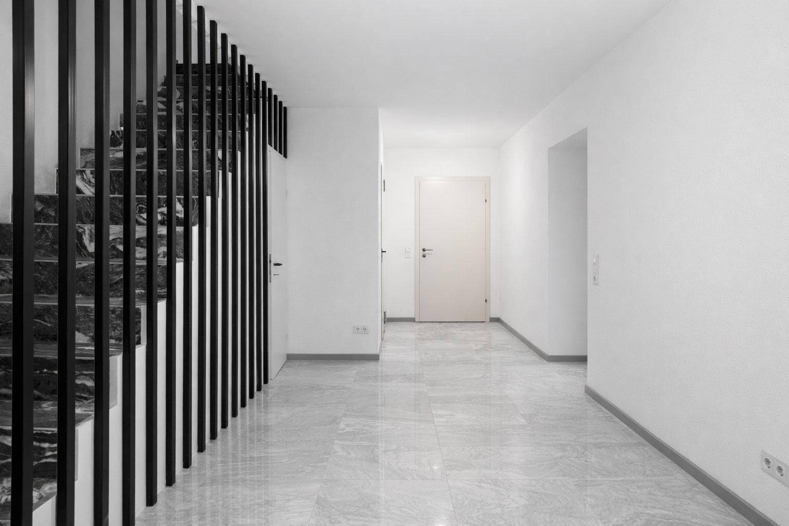 Heller Flur mit moderner Treppe und schwarzer Lamellenwand, die zum Obergeschoss führt.