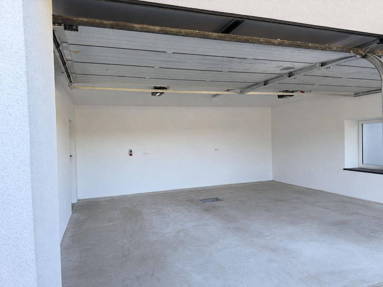 Geräumige Einzelgarage mit Betonboden, weißen Wänden und einem kleinen Fenster für Tageslicht.