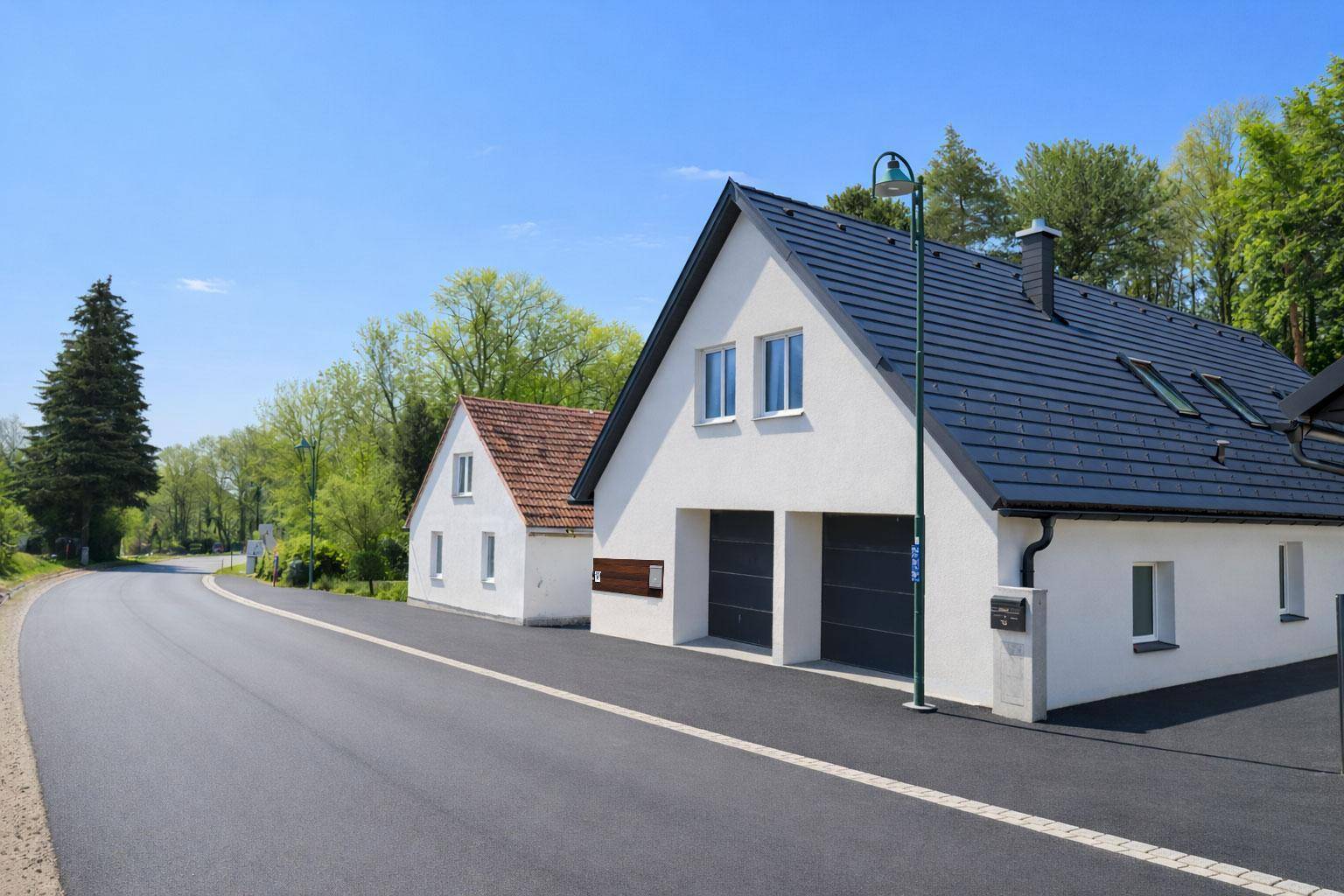 Ansicht des modernen Hauses von der Straße mit angrenzendem Wald und blauem Himmel.