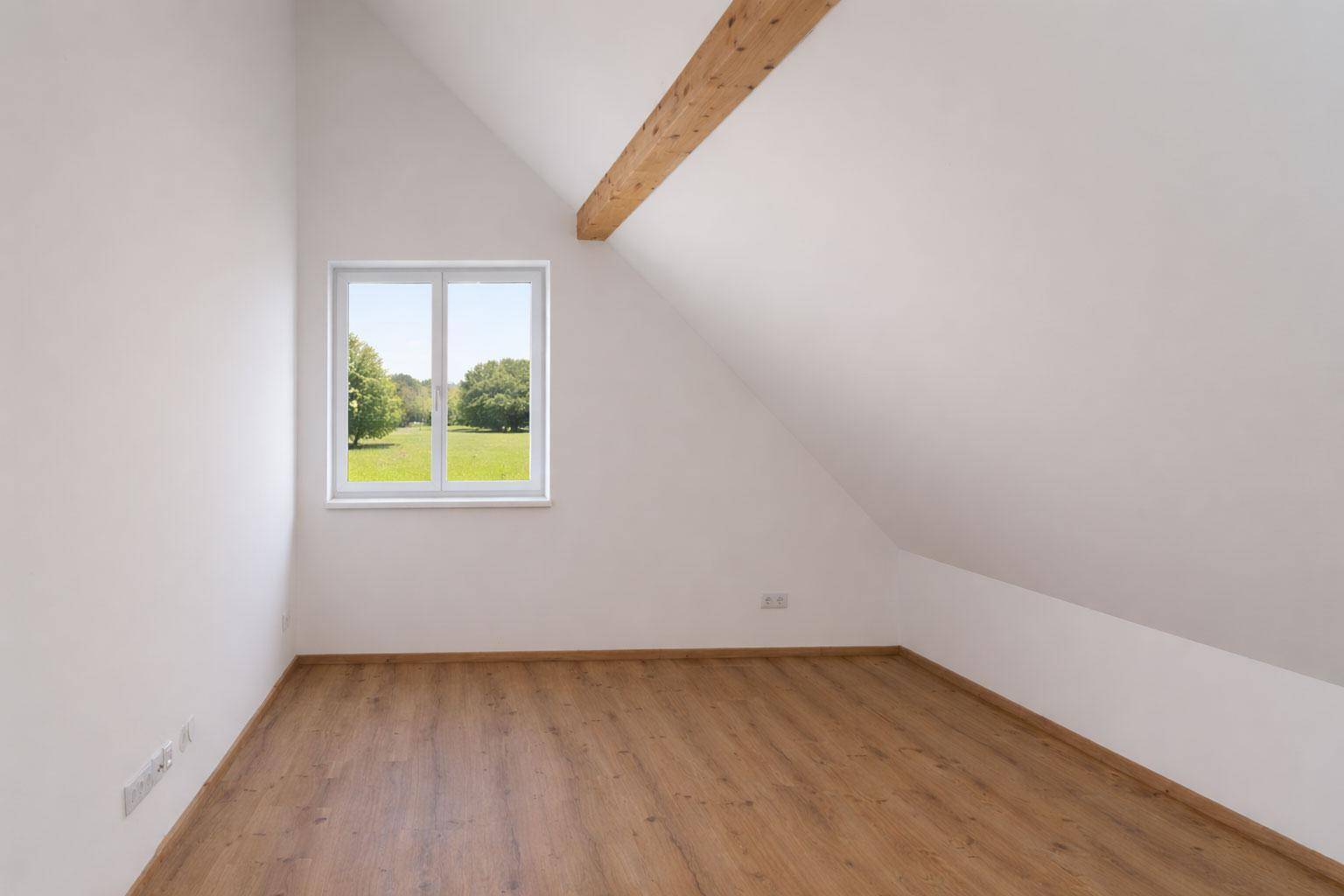 Leeres Schlafzimmer im Dachgeschoss mit Laminatboden und Fenster mit Blick auf die Natur.