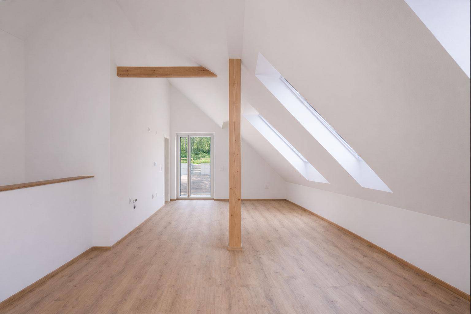 Heller Dachbodenraum mit Holzbalken, Laminatboden und Zugang zu einem Balkon oder Terrasse.