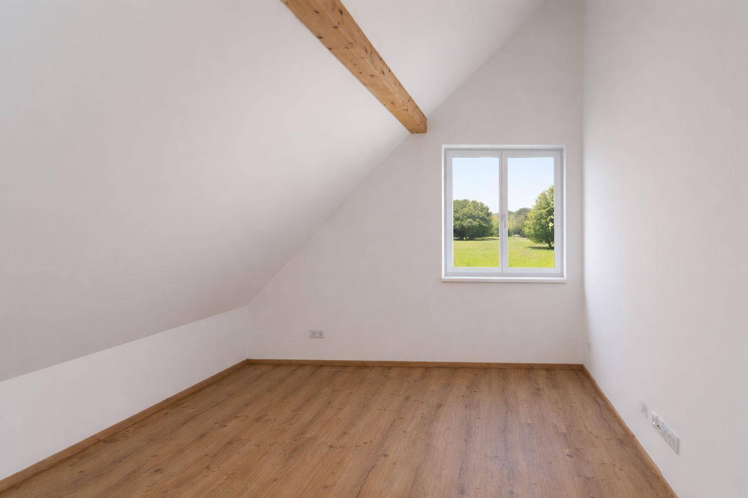Helles Schlafzimmer im Dachgeschoss mit Laminatboden und Fenster mit Blick ins Grüne.