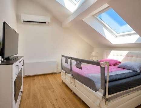 Gemütliches Schlafzimmer im Dachgeschoss mit Holzboden, Dachfenstern und Klimaanlage.
