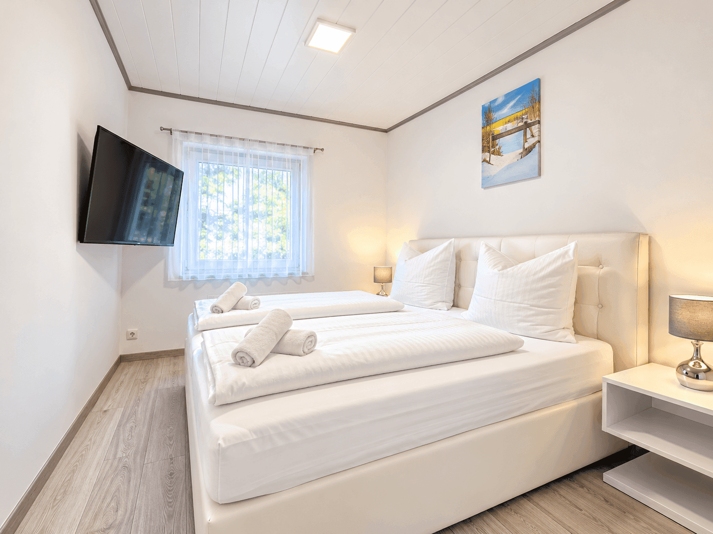 Helles Schlafzimmer mit Doppelbett, Fernseher und Fenster mit Blick ins Grüne.