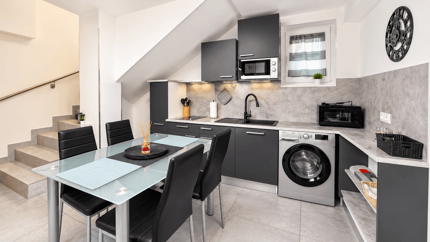 Moderne Küche mit Essbereich, grauen Schränken, integrierter Waschmaschine und Treppenzugang.