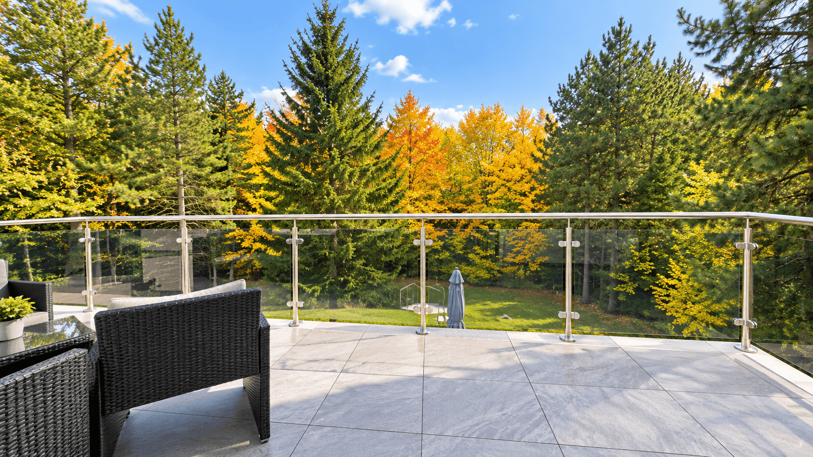 Weitläufiger Balkon mit Glasgeländer und Panoramablick auf den herbstlichen Wald.