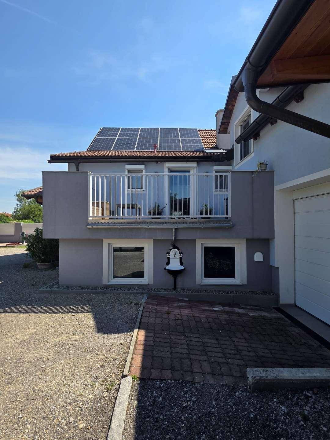 Hausfassade mit Balkon, Solaranlage auf dem Dach und gepflasterter Zufahrt.