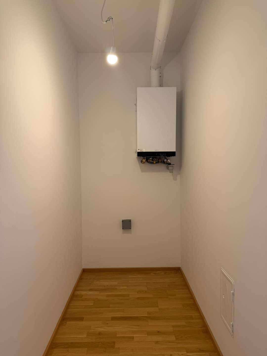 Kleiner Hauswirtschaftsraum mit Heizungsanlage und Holzboden.