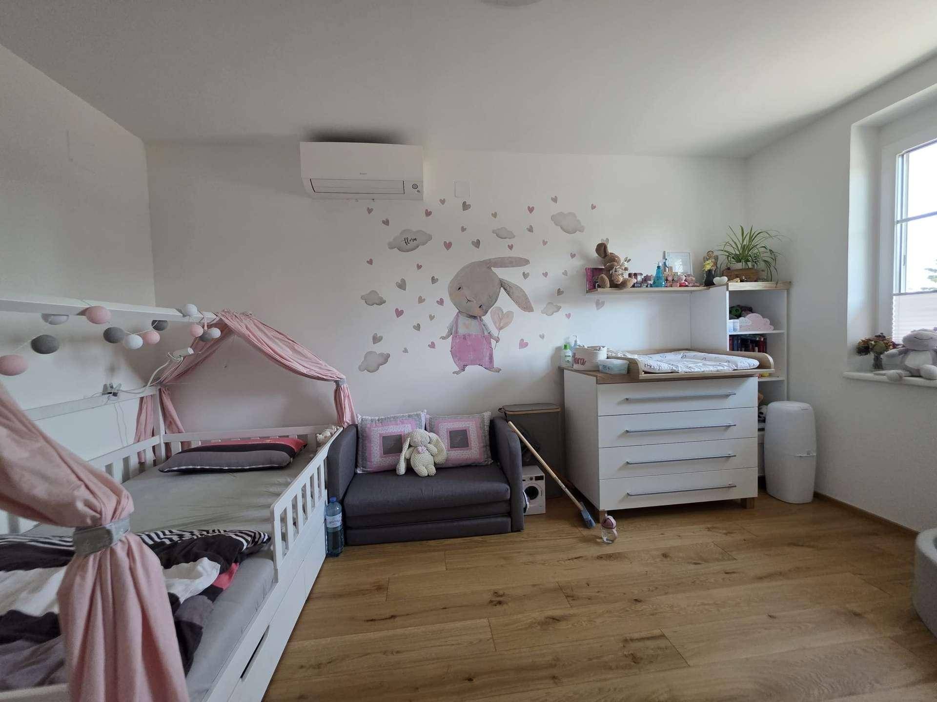 Kinderzimmer mit Holzboden, Fenster und Wanddekoration, ausgestattet mit Klimaanlage.