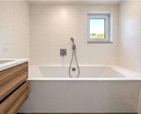 Helles Badezimmer mit Badewanne und Fenster, ausgestattet mit modernen Fliesen.
