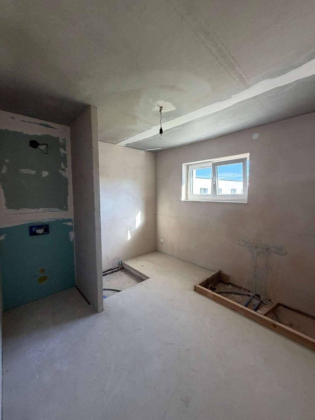 Badezimmer im Rohbau mit Fenster und vorbereiteten Installationen, bereit für den Ausbau.