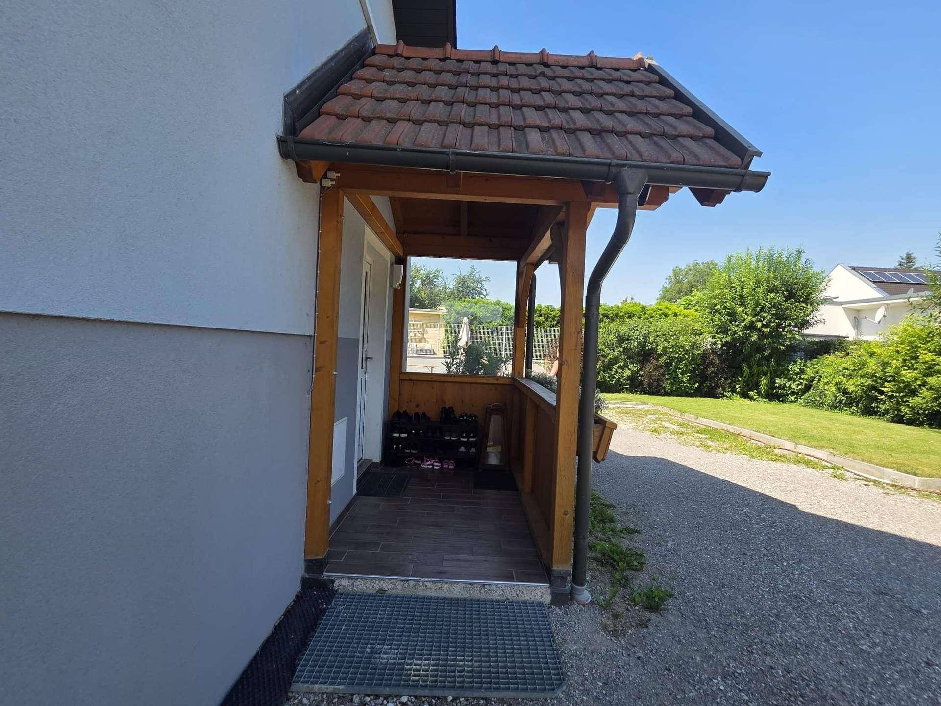 Überdachter Hauseingang mit Holzelementen und Fliesenboden, bietet Schutz vor Witterung.