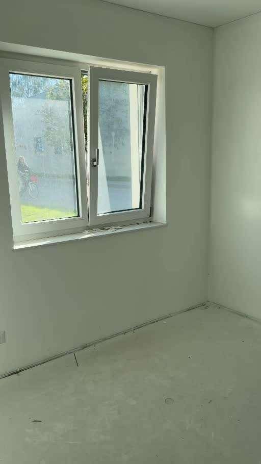 Leerer Raum mit Fenster und unfertigem Boden während der Bauphase, viel Tageslicht.