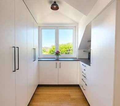 Kleine Küche mit weißen Schränken, Holzboden und Fenster mit Blick ins Grüne.