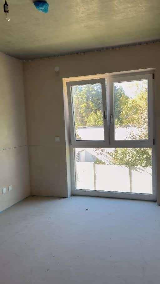 Unfertiger Raum im Rohbau mit großem Fenster und Blick ins Grüne.