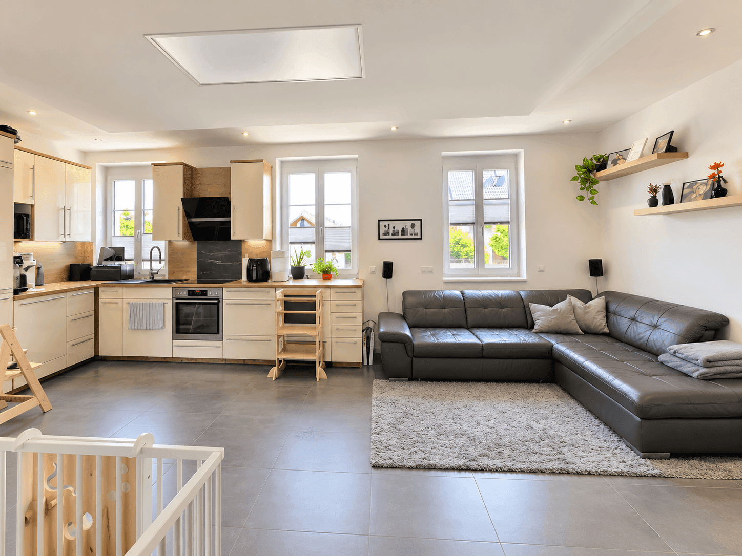Heller offener Wohnbereich mit moderner Einbauküche, großem Sofa und Fliesenboden.