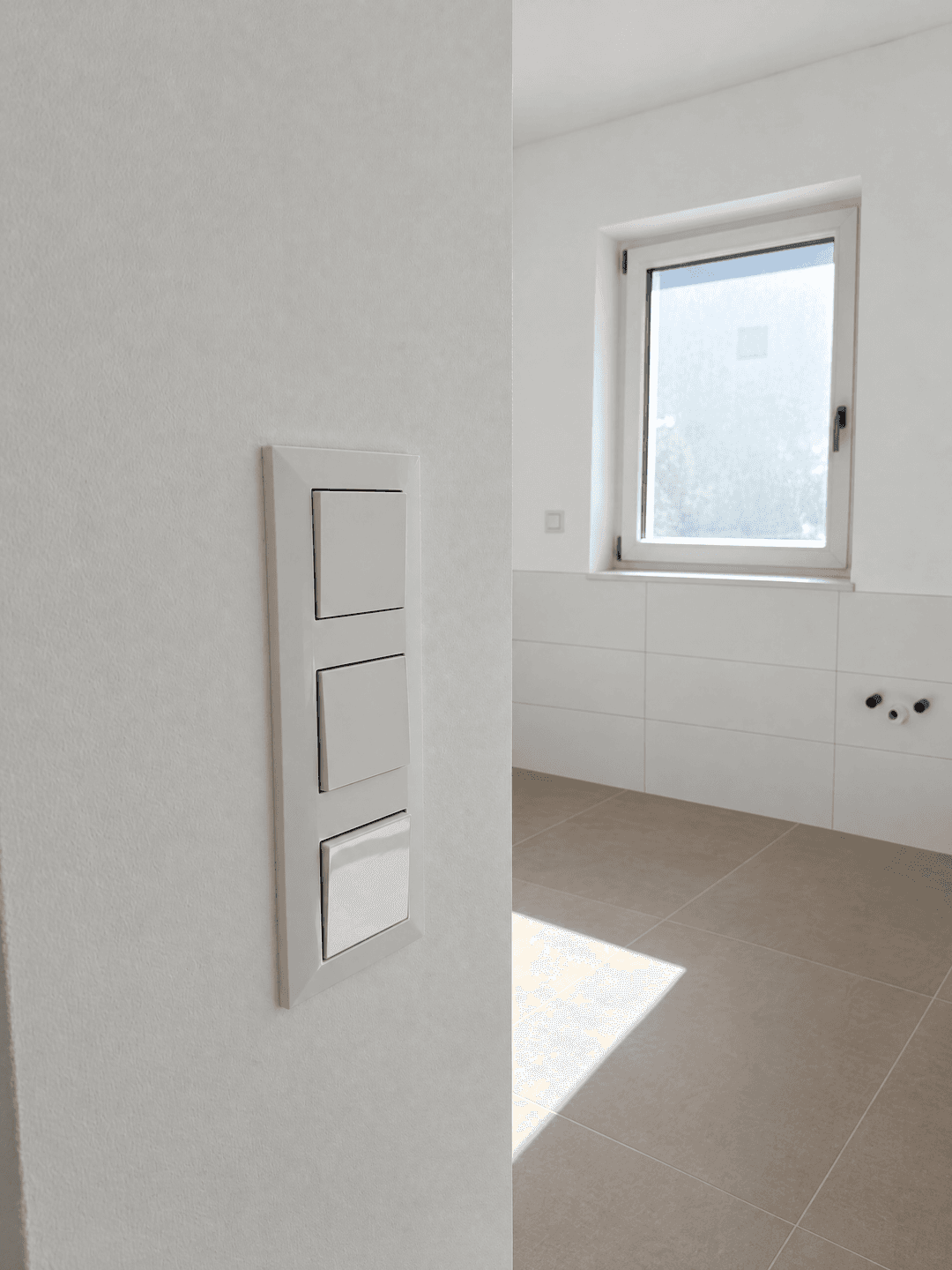 Eingangsbereich zu einem hellen Badezimmer mit Fliesenboden und Fenster.