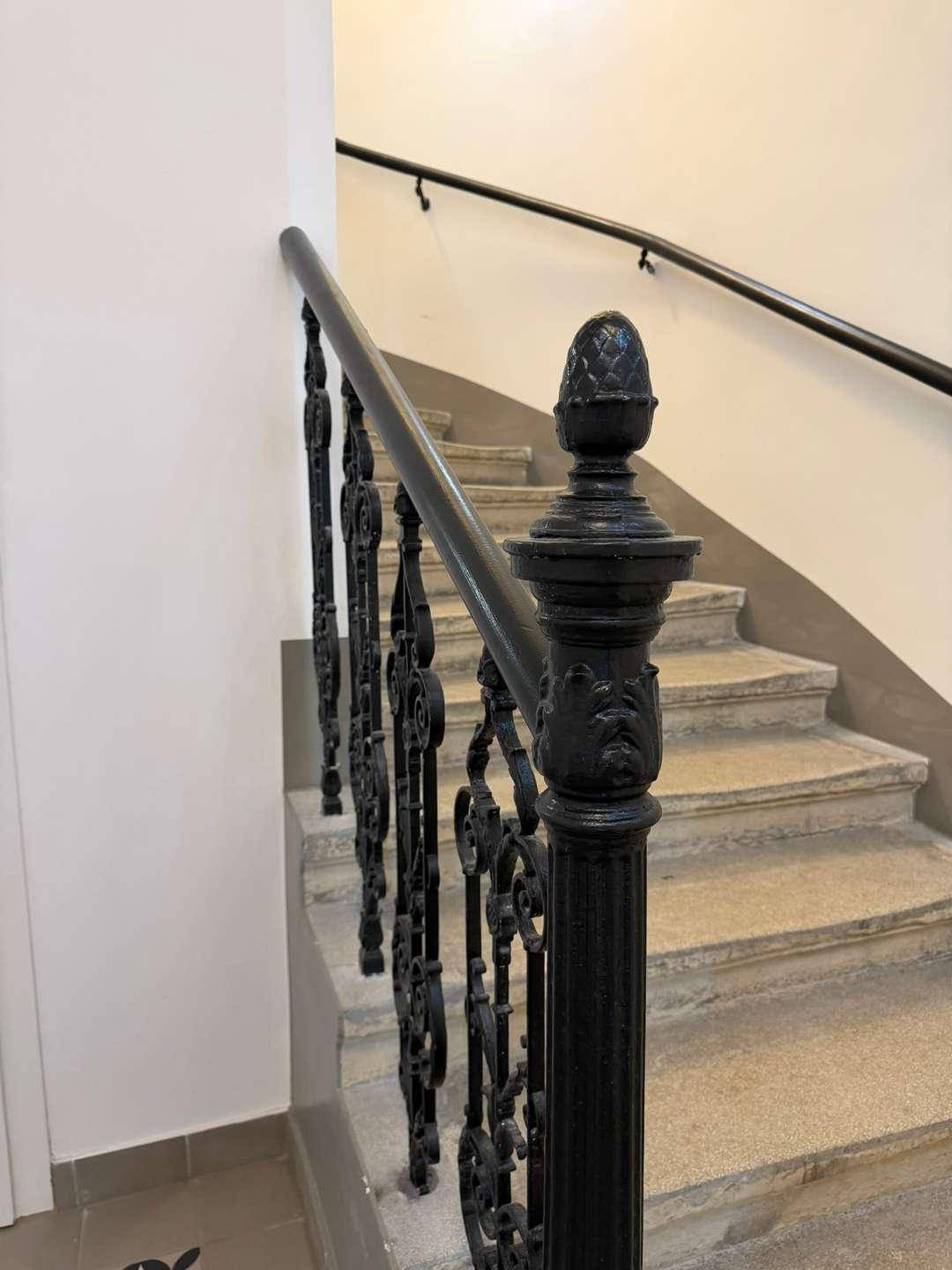 Historisches Treppenhaus mit kunstvollem schmiedeeisernem Geländer und Steinstufen.