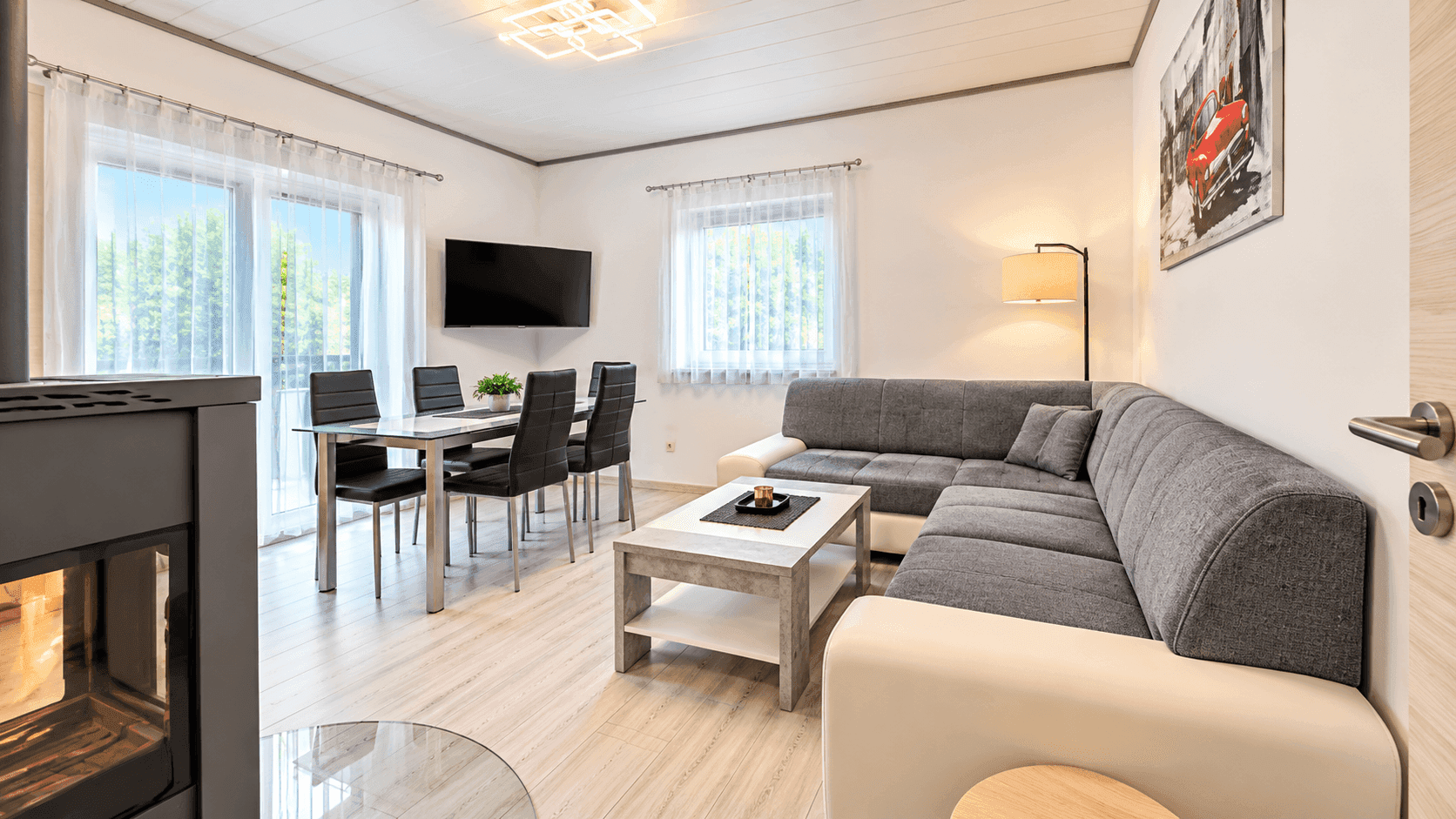 Gemütlicher Wohn-Essbereich mit Kaminofen, großem Sofa und Zugang zum Balkon.