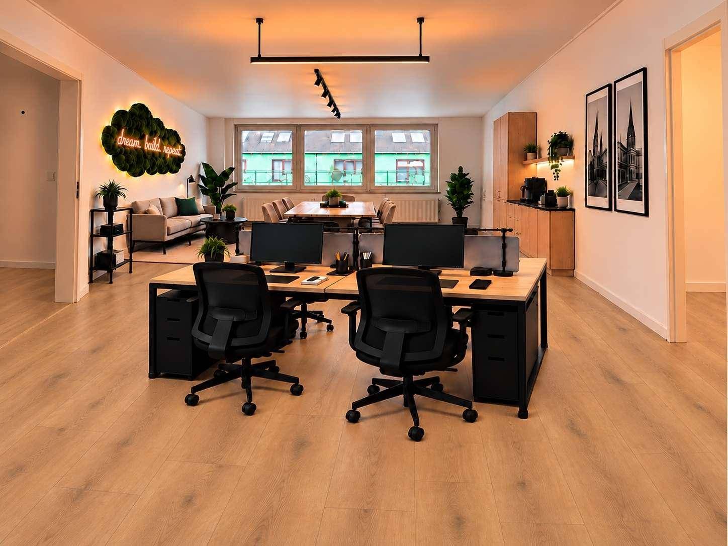 Offener Bürobereich mit mehreren Arbeitsplätzen und einem entspannten Lounge-Bereich im Hintergrund.