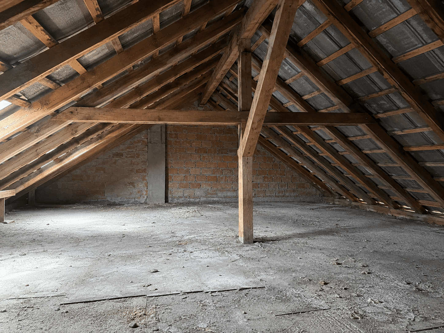 Dachboden mit robuster Holzbalkenkonstruktion und Ziegelwänden, durch ein Dachfenster hell beleuchtet.