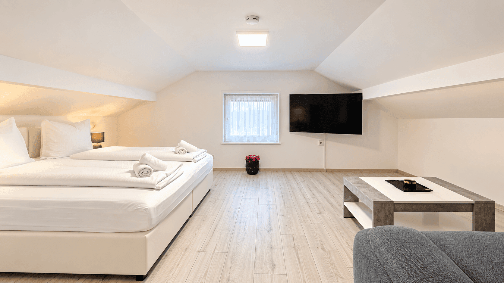 Helles Schlafzimmer im Dachgeschoss mit zwei Einzelbetten, Holzboden und Fernseher.