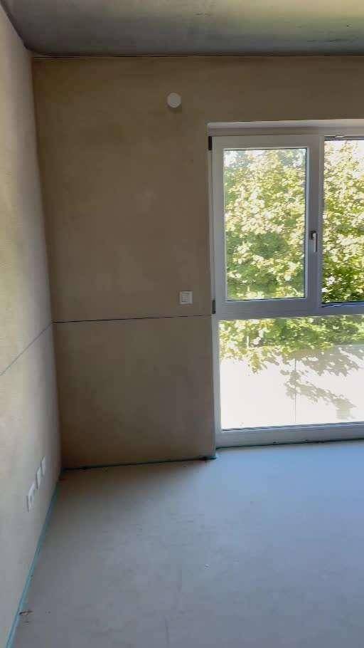 Unfertiger Raum im Rohbau mit großem Fenster und Blick ins Grüne.