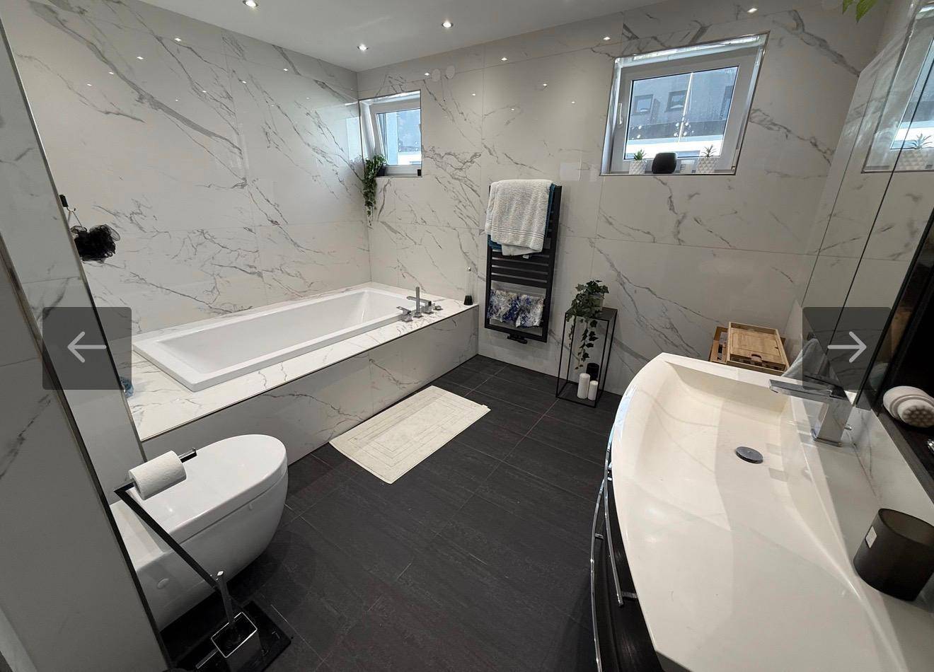 Modernes Badezimmer mit Badewanne, breitem Einzelwaschbecken und Marmoroptik-Fliesen.