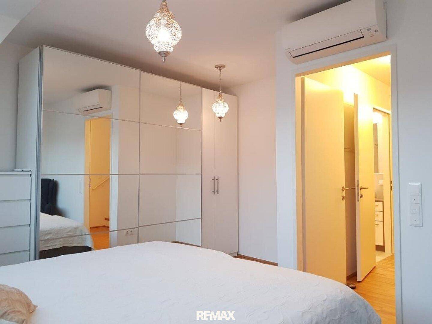 Modernes Schlafzimmer mit großem Bett, verspiegelten Einbauschränken und Klimaanlage.
