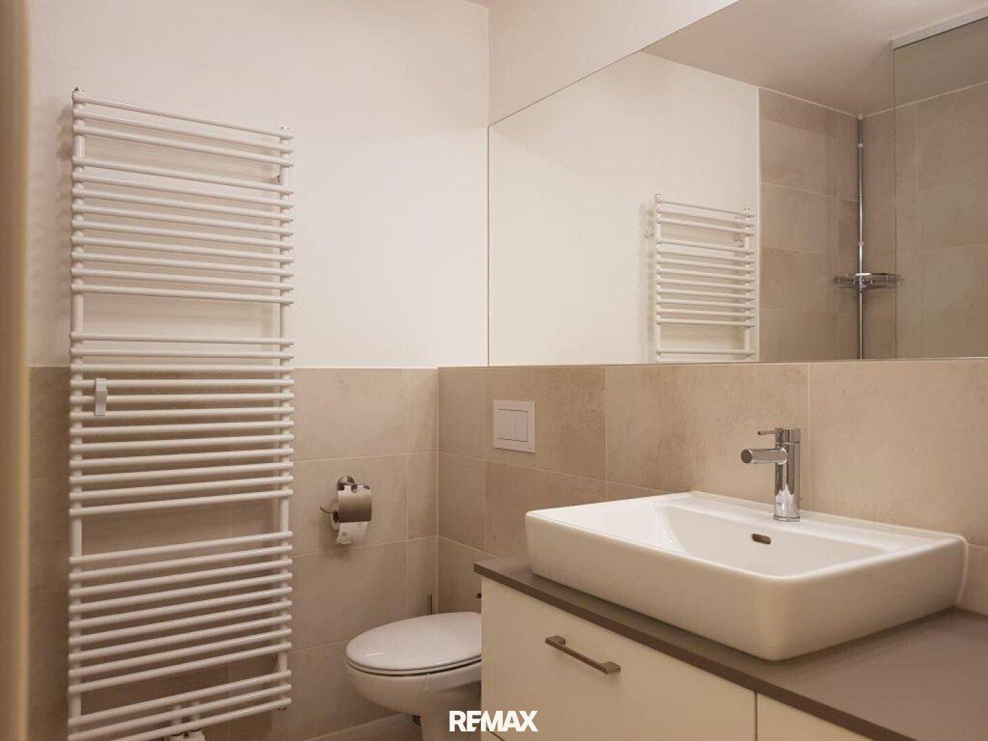 Modernes Badezimmer mit Waschtisch, WC, beheiztem Handtuchhalter und hellen Fliesen.