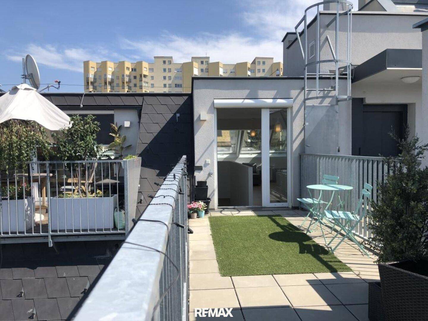 Sonnige Dachterrasse mit Kunstrasen, Sitzgelegenheiten und Blick auf die umliegenden Gebäude.