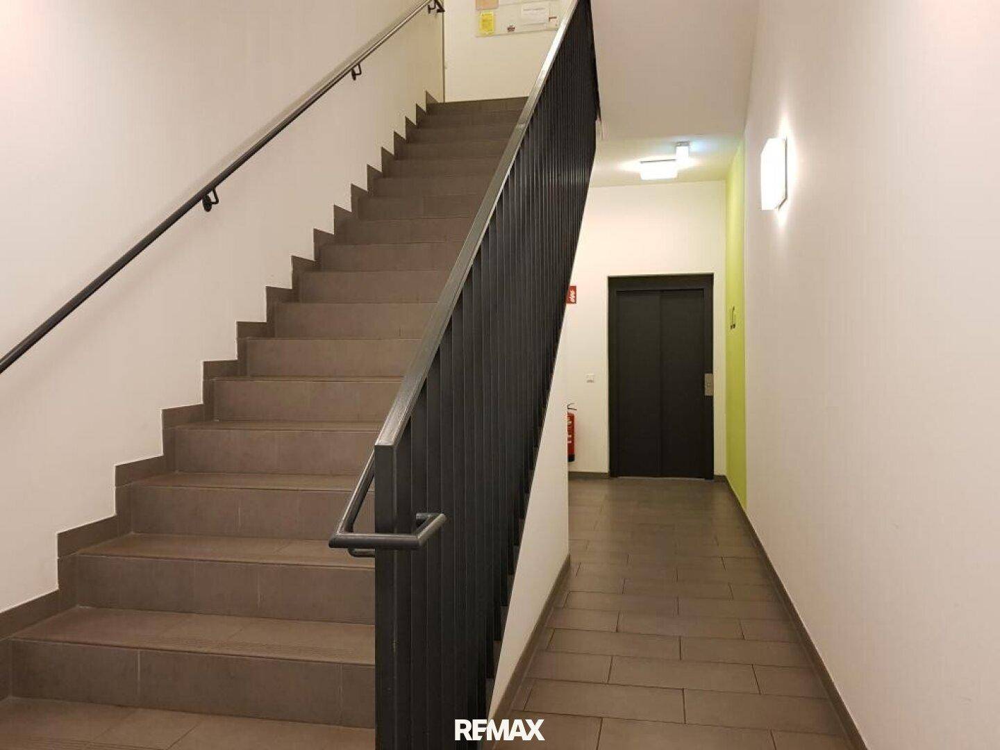 Treppenhaus mit robusten Stufen, Geländer und Zugang zum Aufzug im Gebäude.