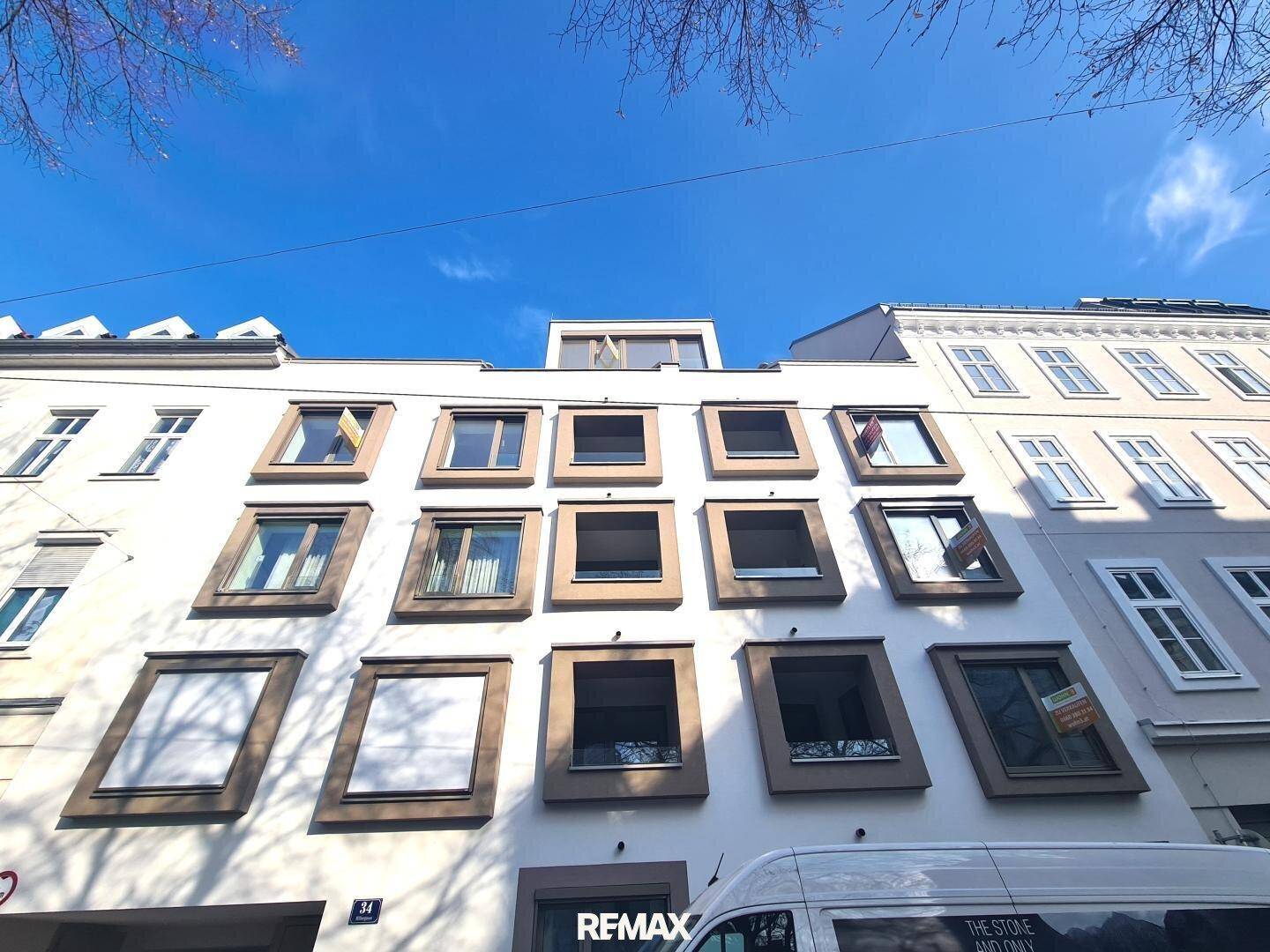 Moderne Gebäudefassade mit zahlreichen Fenstern und Jalousien unter einem klaren blauen Himmel.