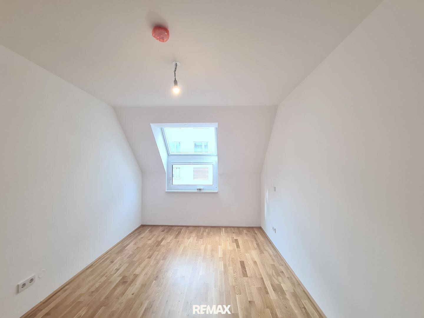 Ruhiges Schlafzimmer mit Holzboden, weißen Wänden und einem Dachfenster, das für eine angenehme Atmosphäre sorgt.