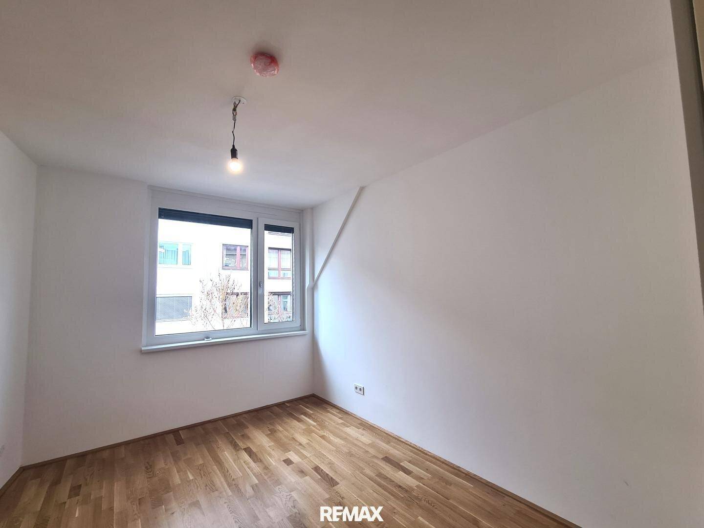Geräumiges Schlafzimmer mit Holzboden, weißen Wänden und einem großen Fenster für optimale Belichtung.