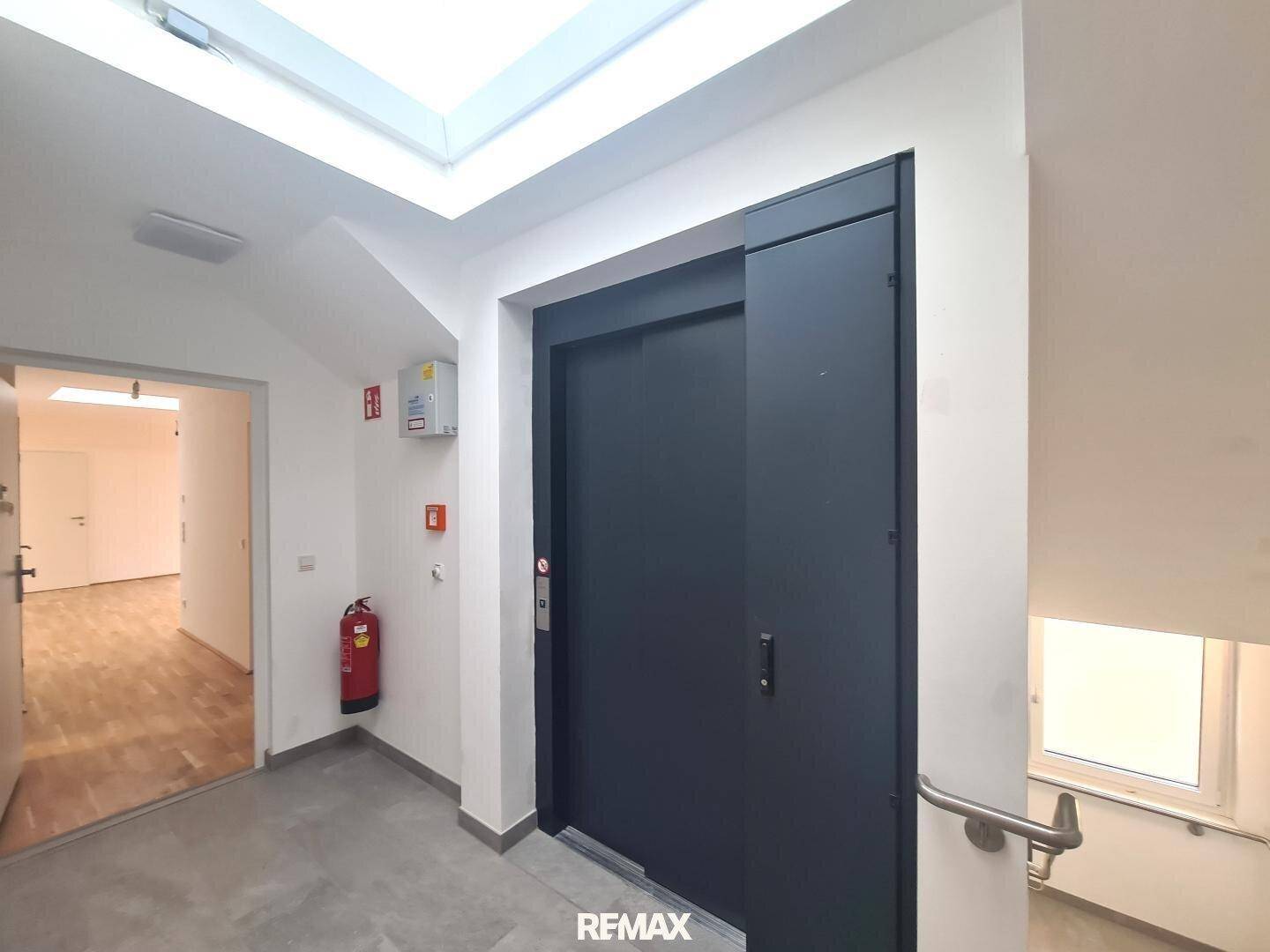 Heller Eingangsbereich mit Aufzug, Treppe und einem Oberlicht, das Tageslicht spendet.
