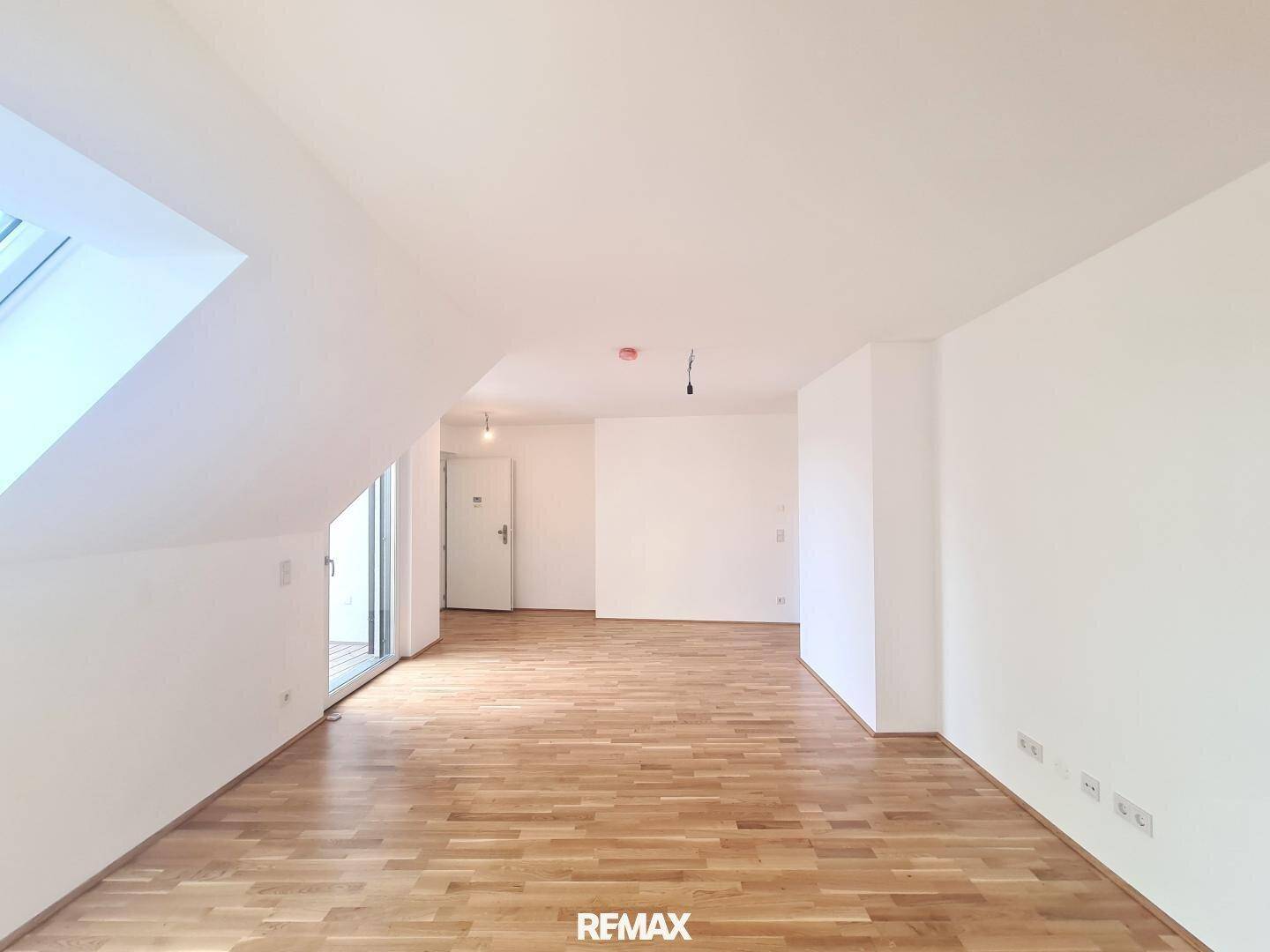 Heller, leerer Raum mit Holzboden, weißen Wänden und Zugang zu einer Terrasse, ideal für ein Wohnzimmer.
