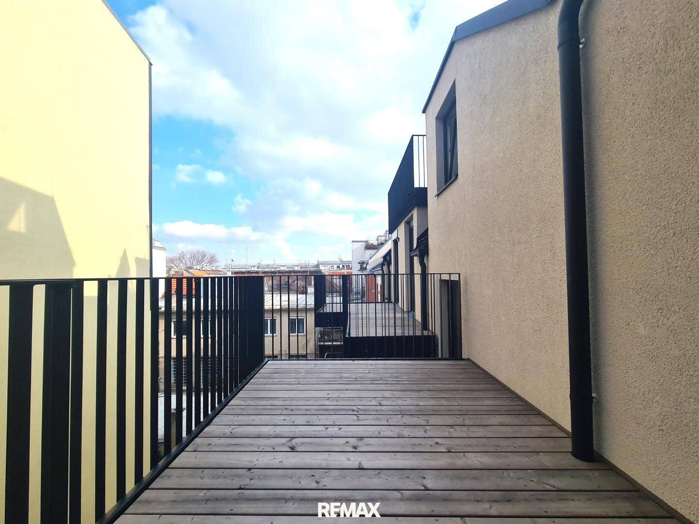 Geräumige Holzterrasse mit schwarzem Geländer und Blick auf die umliegenden Gebäude.