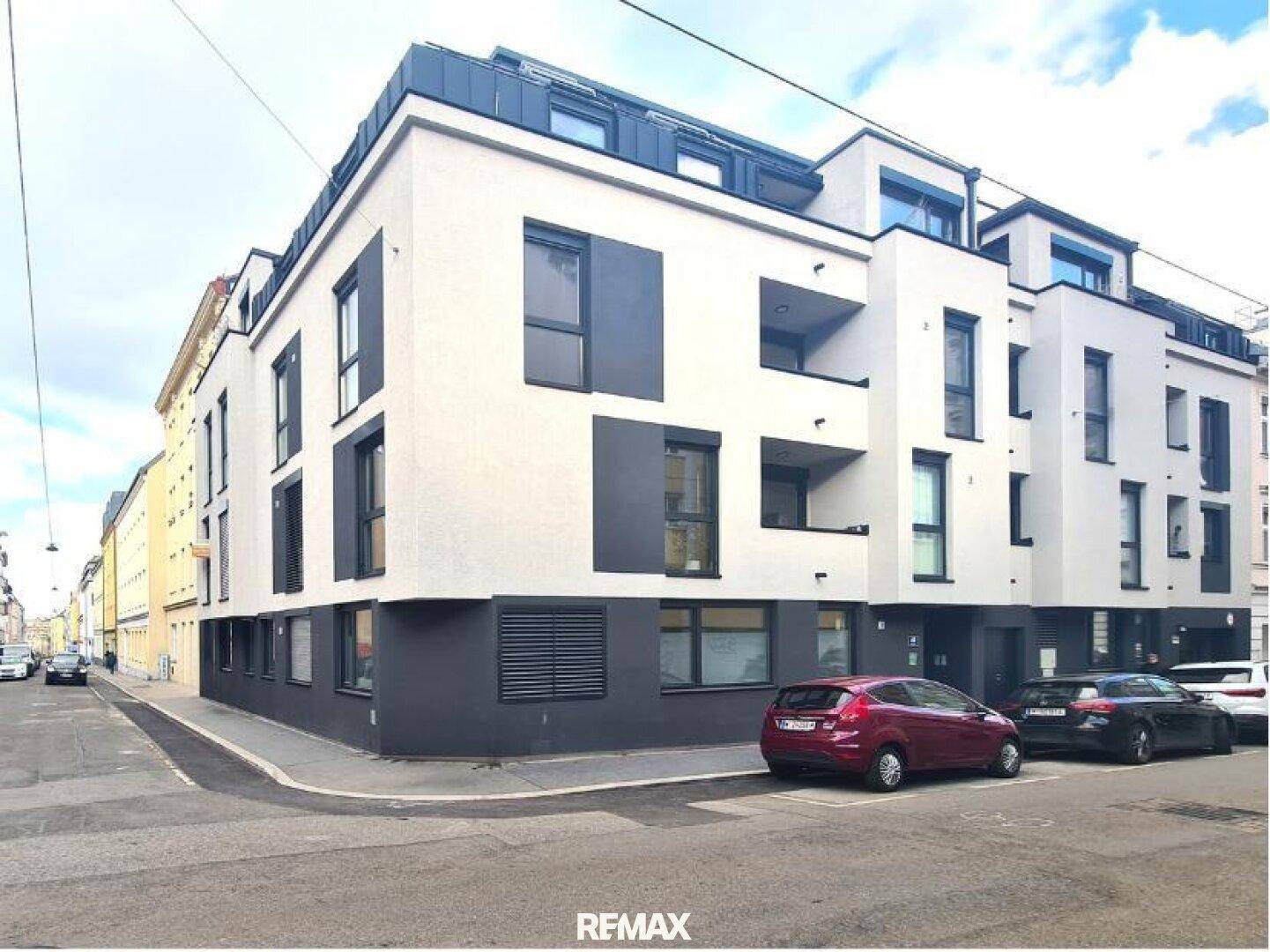 Moderne Wohnhausfassade mit klaren Linien und großen Fenstern an einer städtischen Straße.