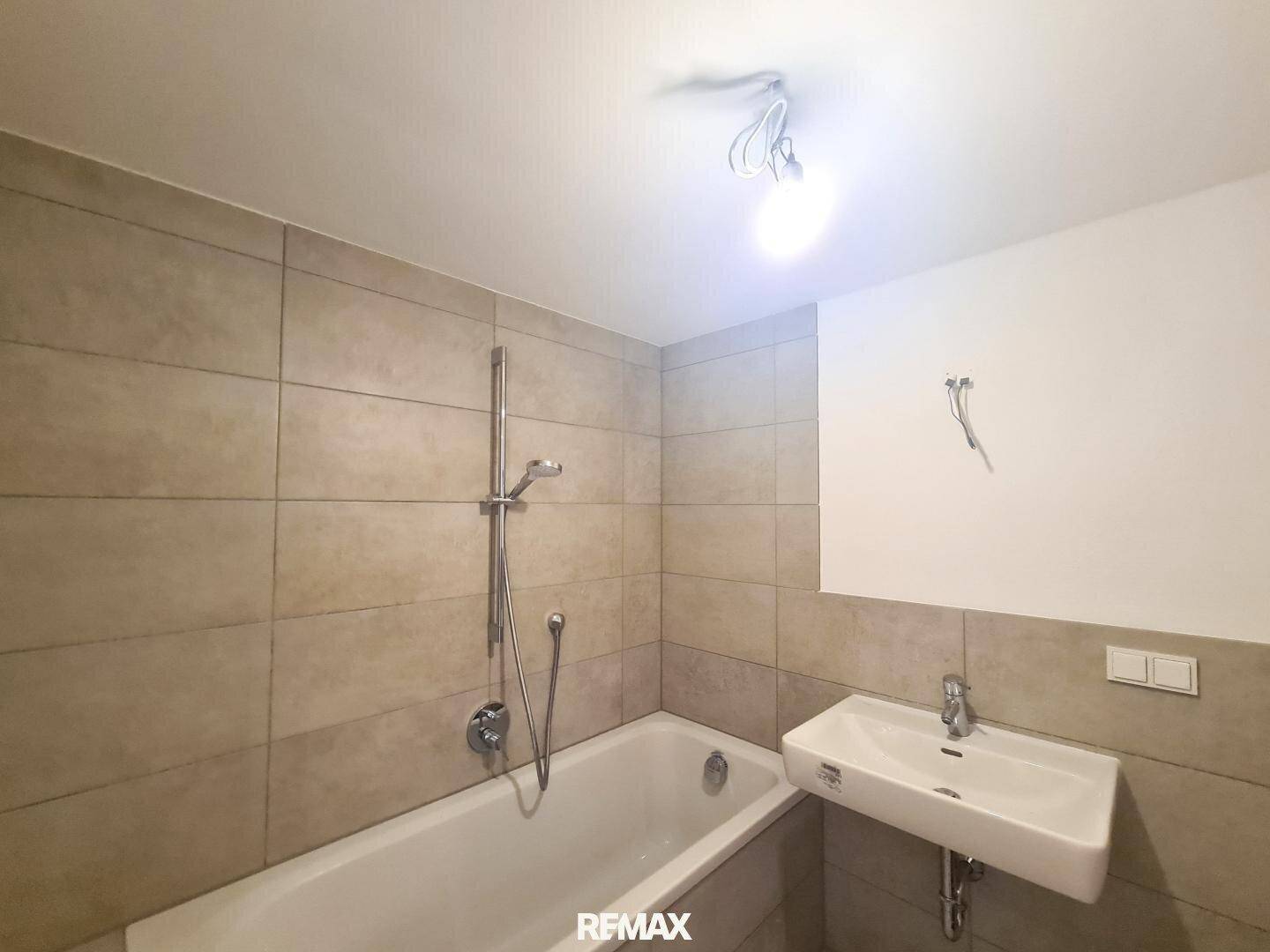 Modernes Badezimmer mit Badewanne, Duscharmatur, Waschbecken und beigefarbenen Fliesen.