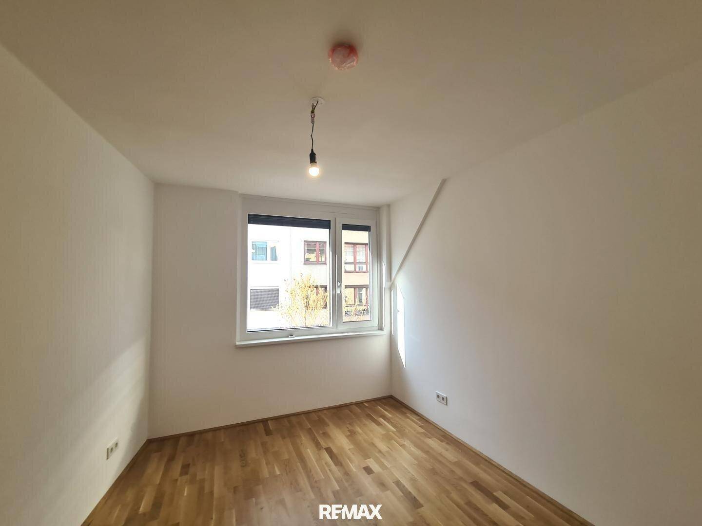 Helles Schlafzimmer mit Holzboden, weißen Wänden und einem großen Fenster, das viel Licht spendet.
