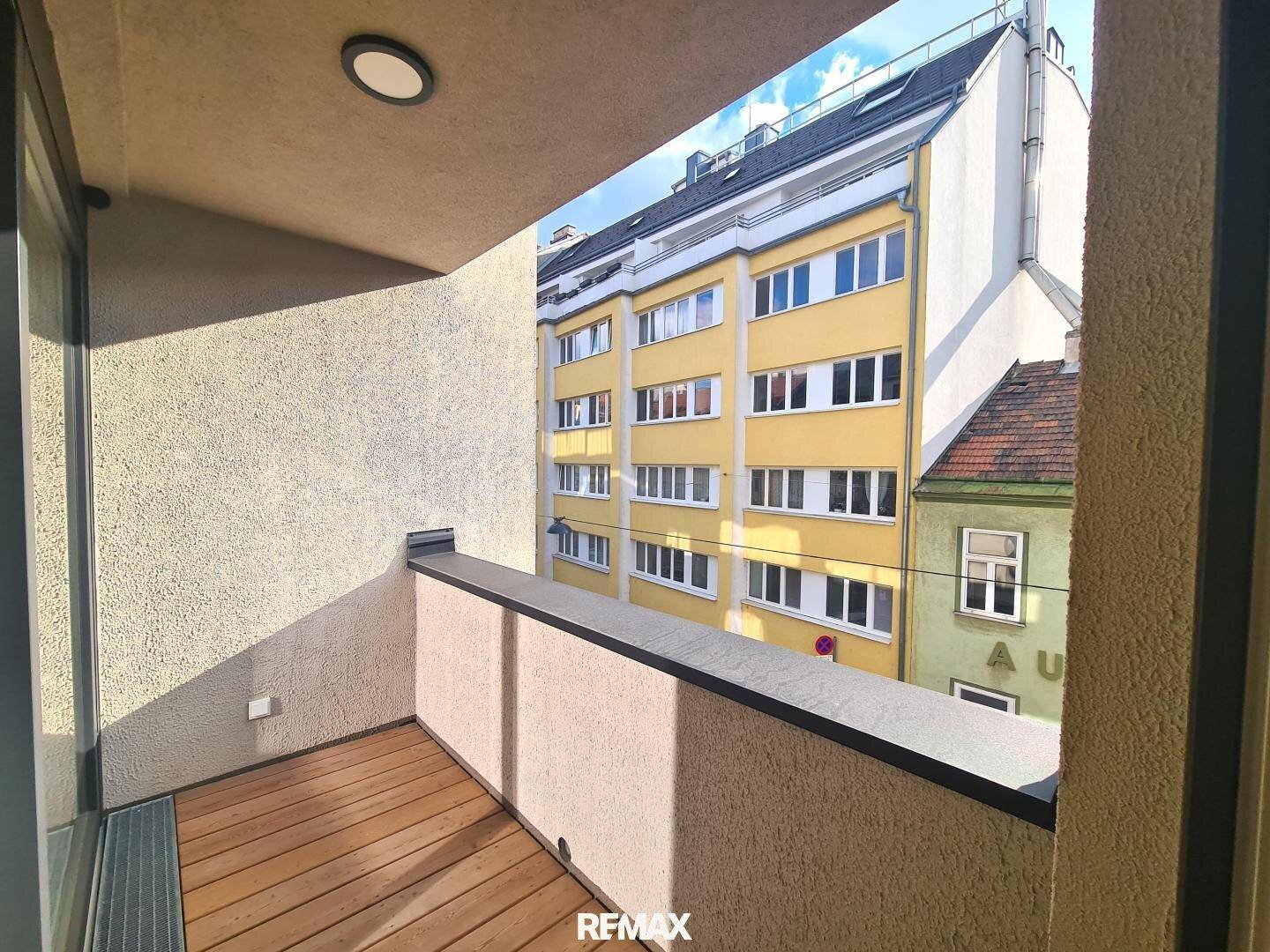 Kleiner Balkon mit Holzboden und Blick auf die umliegenden Gebäude der Stadt.