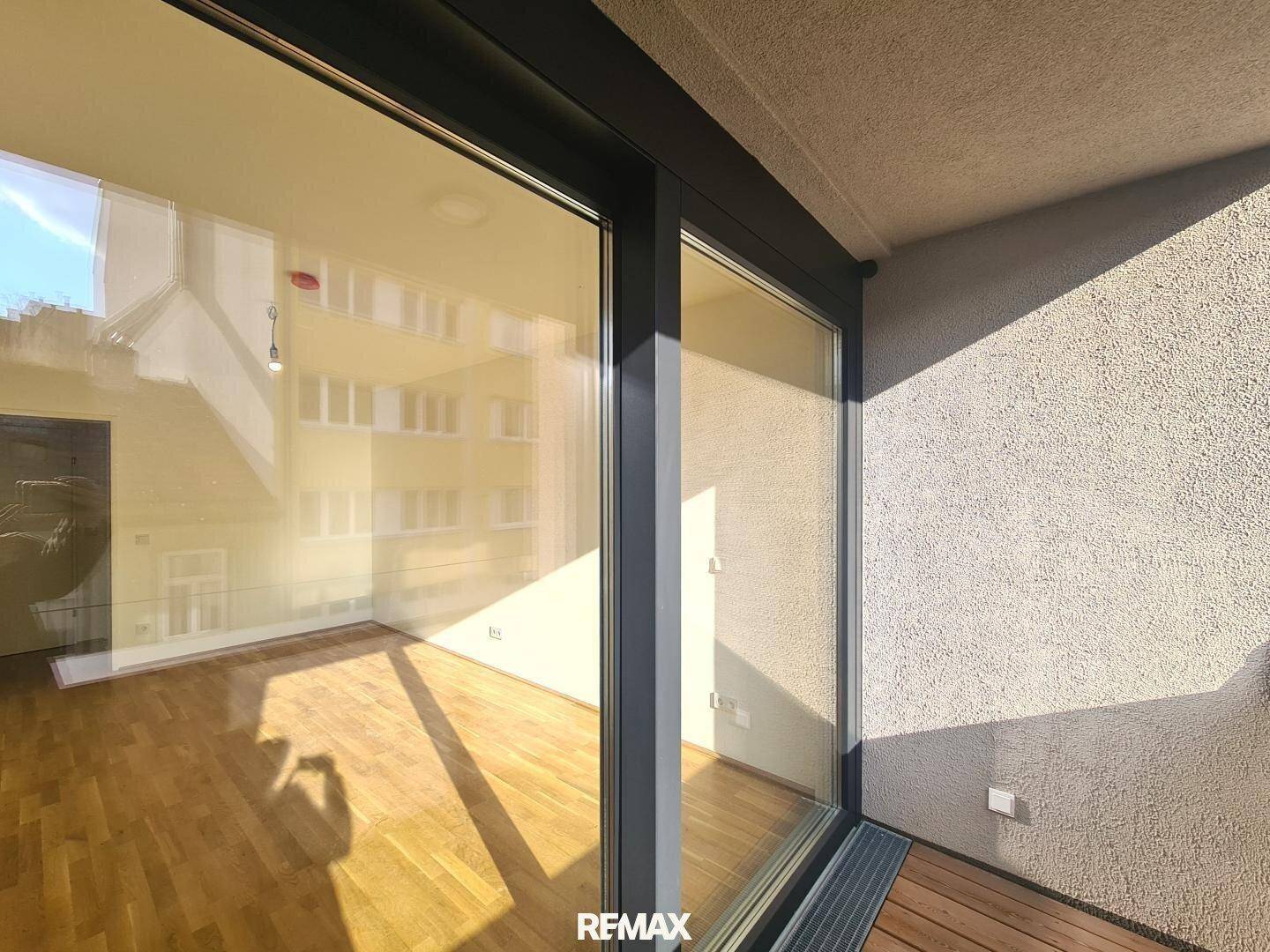 Blick vom Balkon auf die umliegenden Gebäude, mit großen Glasfenstern zum Innenraum.