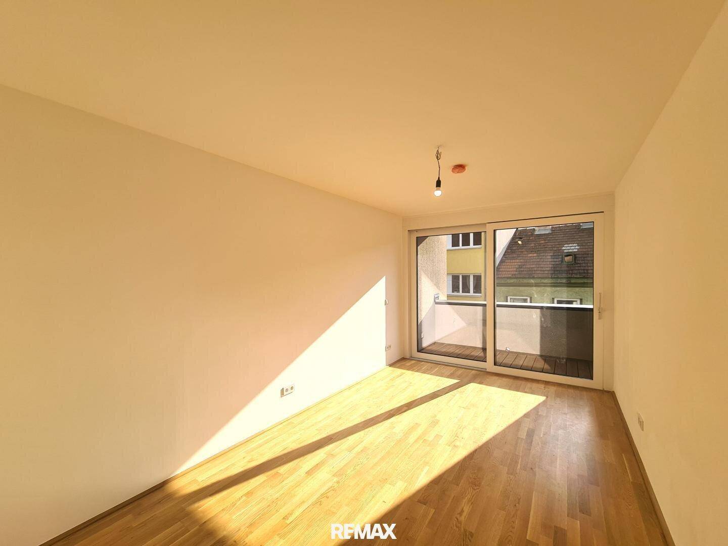 Lichtdurchfluteter Raum mit Holzboden und Zugang zu einem Balkon, ideal für einen Wohnbereich.