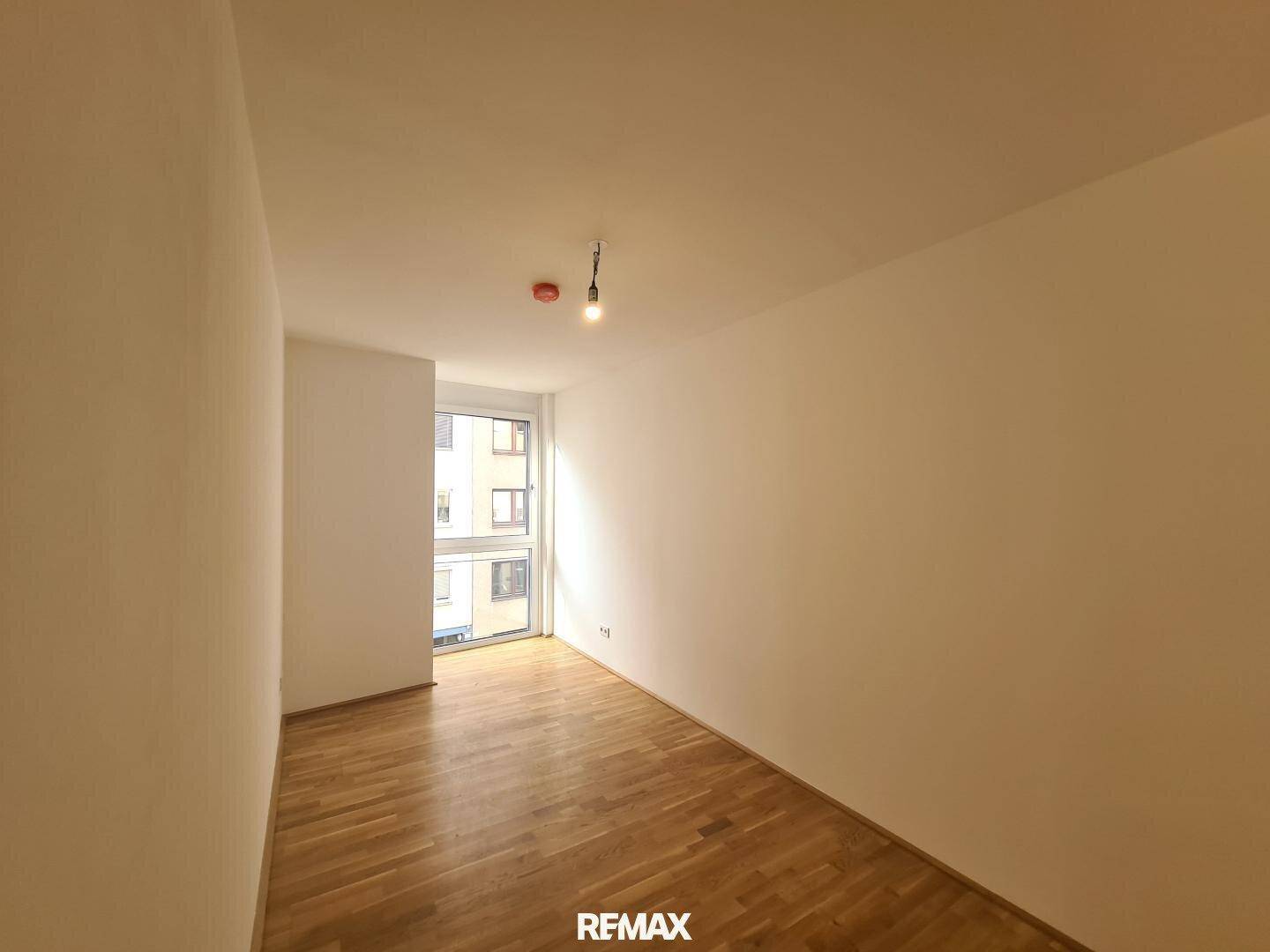 Kleineres Zimmer mit Parkettboden und einem Fenster, das viel Sonnenlicht hereinlässt.